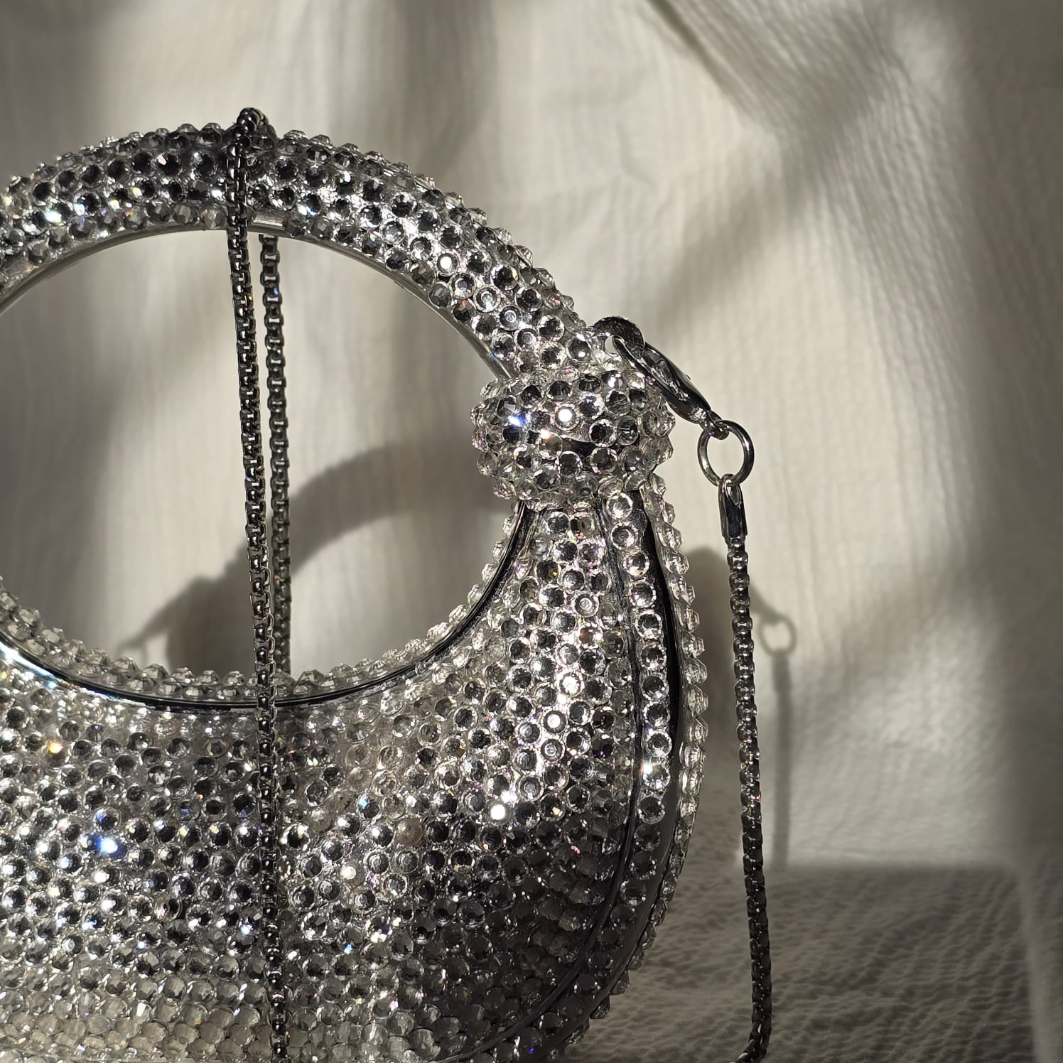 Handcrafted silver rhinestone evening purse in a modern crescent shape with a circular handle, showcasing premium crystal craftsmanship in warm lighting.