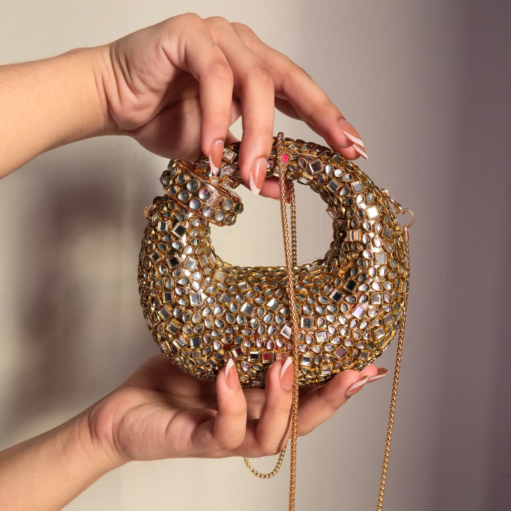 Close-up of a person holding a sparkling gold rhinestone evening purse, highlighting the intricate jewel placement and curved handle.