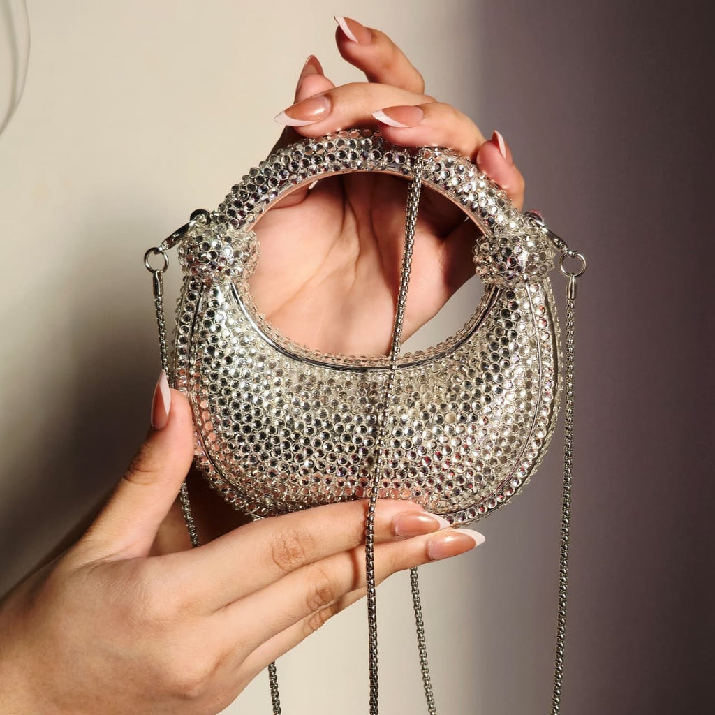 Close-up of a hand holding the sparkling silver crystal bag, demonstrating the product size and the intricate detail of the jewel embellishments.