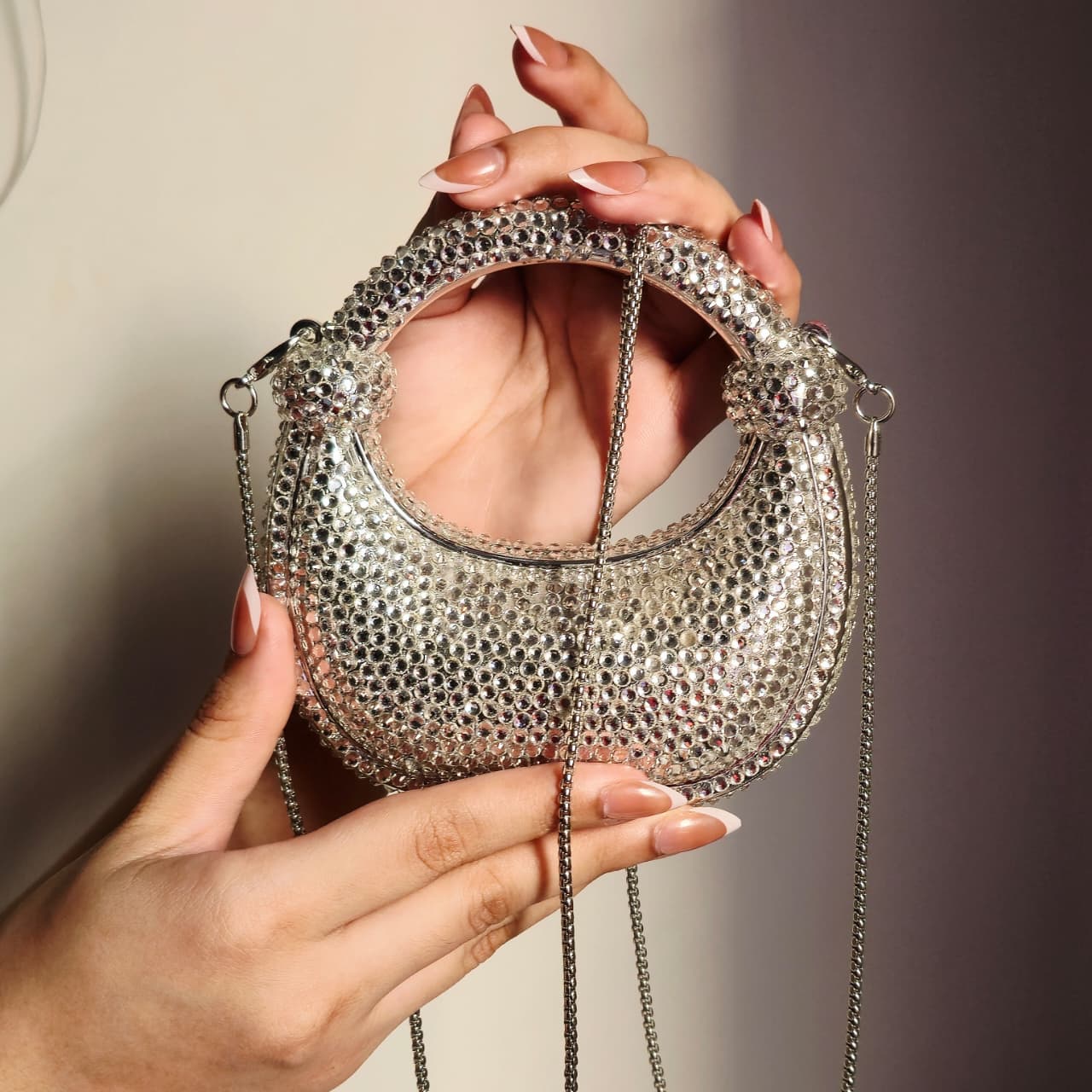 Close-up of a hand holding the sparkling silver crystal bag, demonstrating the product size and the intricate detail of the jewel embellishments.