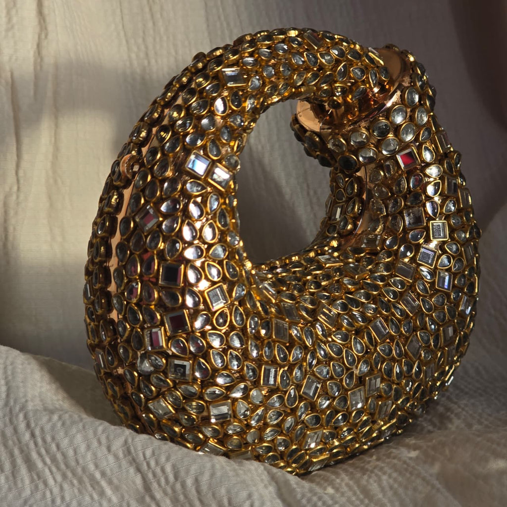 Side angle of a structured gold crystal handbag showing the 3D depth and reflective shine of the mirror embellishments.
