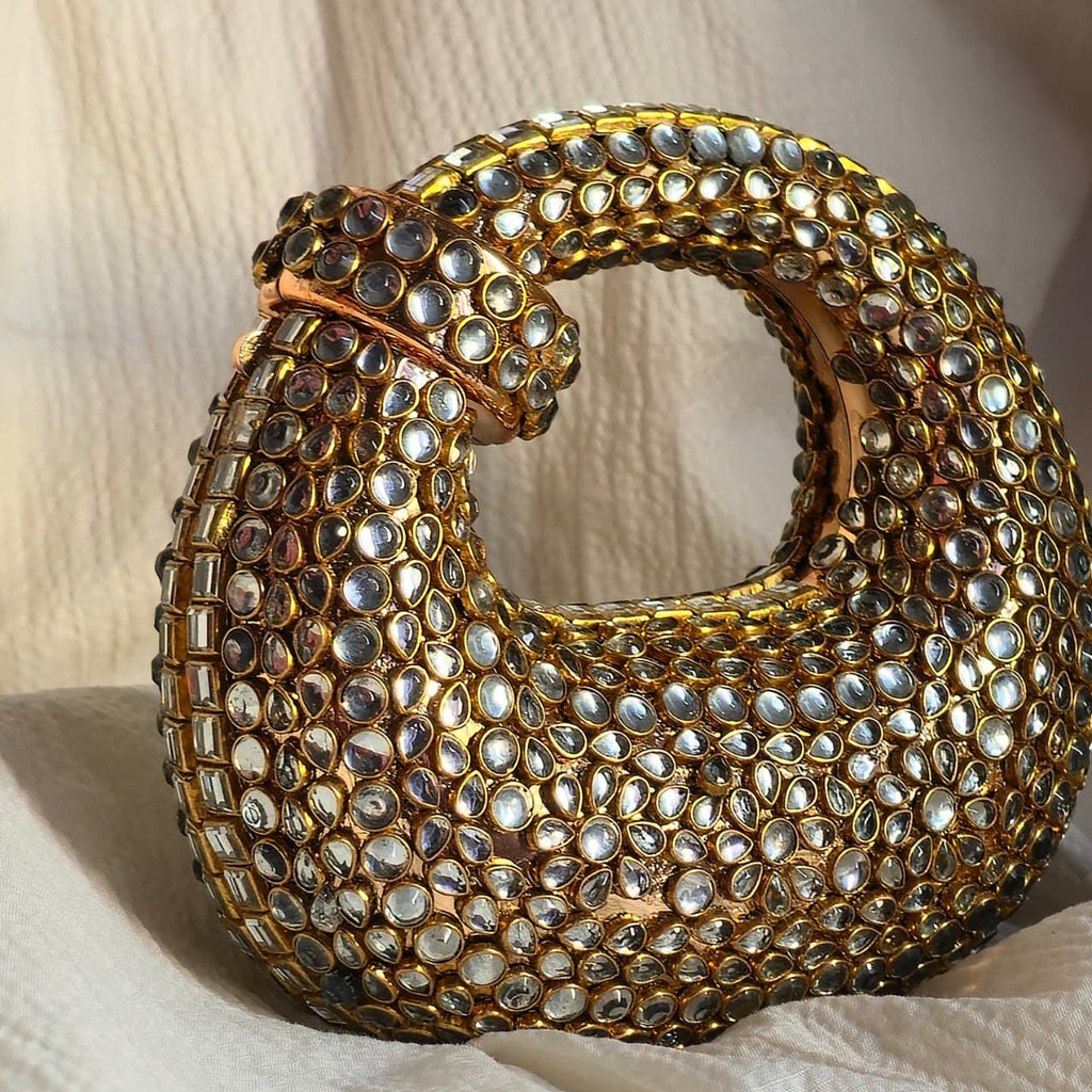 Side view of the structured gold crystal handbag sitting upright, highlighting the reflective shimmer and curved silhouette.