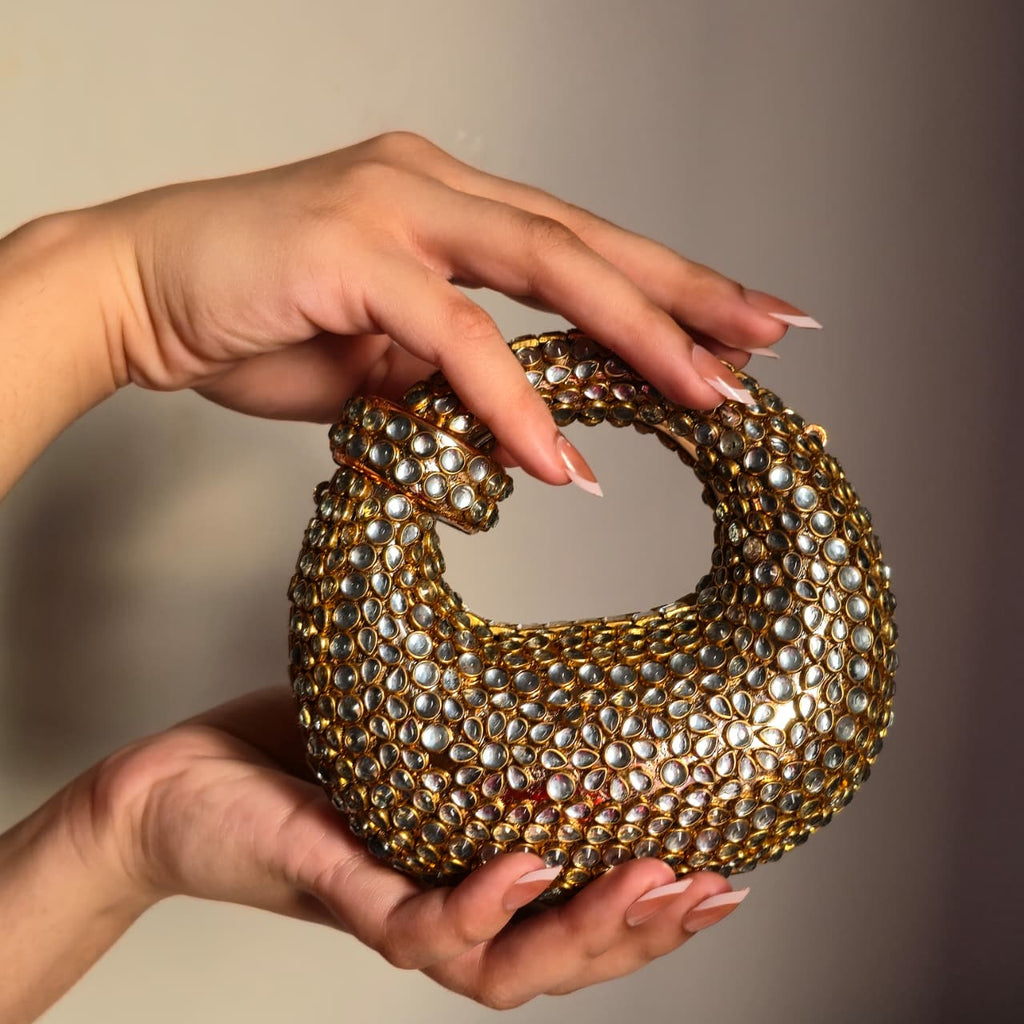 Close-up of two hands holding the gold mirror clutch, showcasing the intricate jewel placement and the compact size of the evening purse.