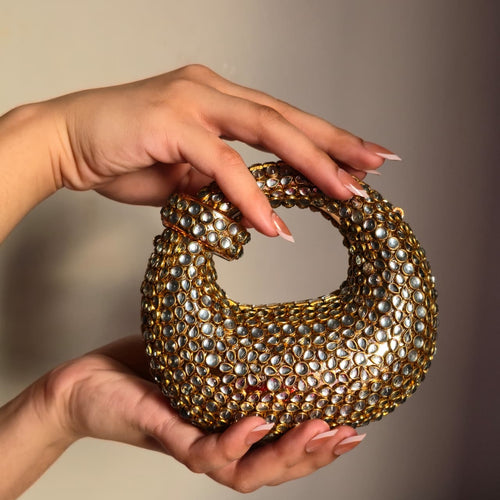Close-up of two hands holding the gold mirror clutch, showcasing the intricate jewel placement and the compact size of the evening purse.
