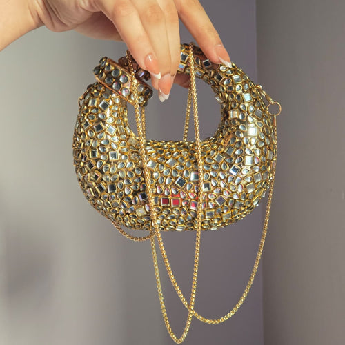 A hand holding a small gold embellished evening bag by its chain strap to show the product size and scale.