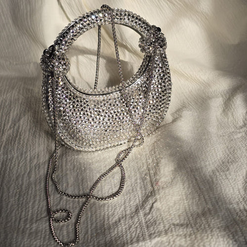 Angled side view of a silver rhinestone hobo-style handbag showing its structured curve and light-reflecting crystal exterior.
