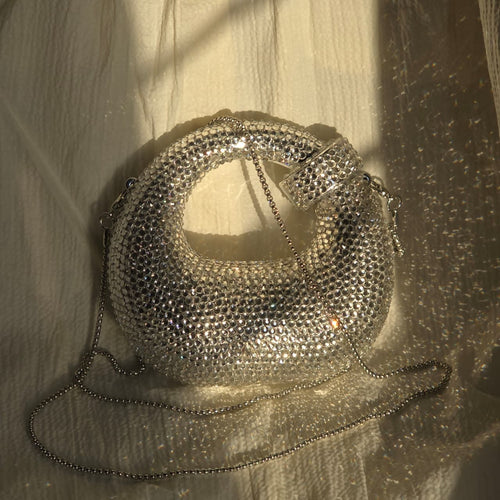 Silver rhinestone mini bag lying flat — handcrafted 
crystal embellished clutch by Prisms & Petale Karachi.